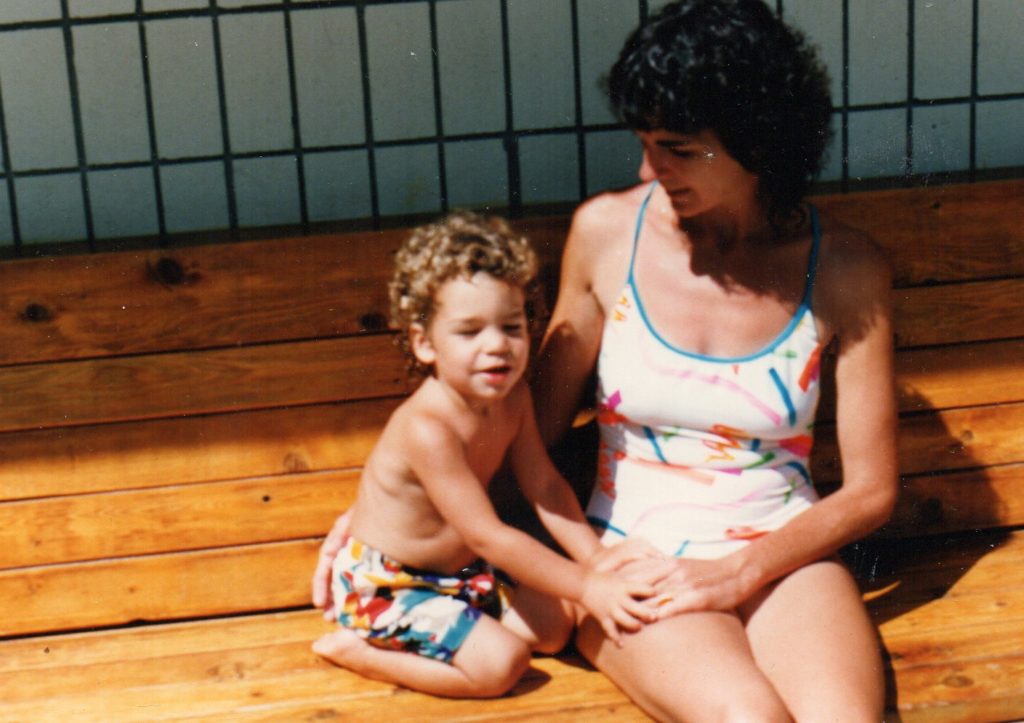 little boy in shorts on a patio with his mother in her swimsuit