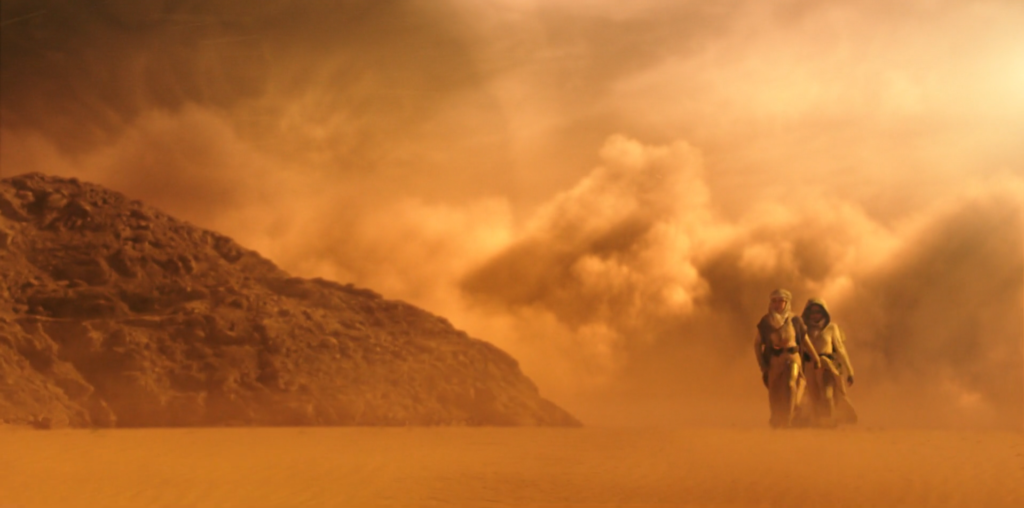 Georgiou and Burnham walking through a desert with a storm in the background.