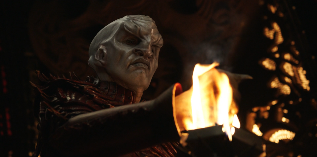 Voq, a Klingon, puts his hand in a ceremonial flame.
