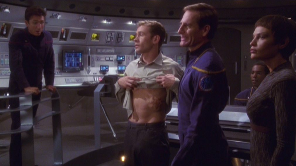 Trip has to lift up his shirt to show his pregnancy to the Klingons