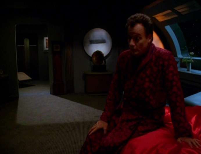 Q sits on the edge of Janeway's bed in "The Q and the Grey"