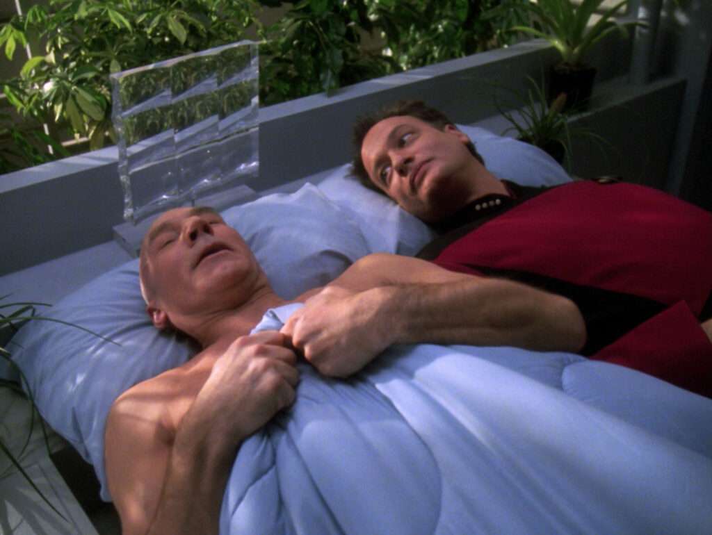 Picard naked in bed under a sheet, with Q lying beside him in a starfleet uniform, from "Tapestry"
